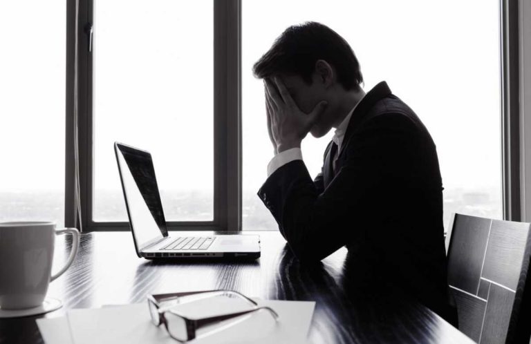 Man, looking at a computer, holding his face in frustration over his business debt